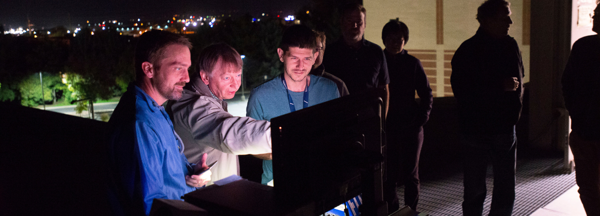 Members of the AWE research team gathered around a computer monitor on a rooftop at night.